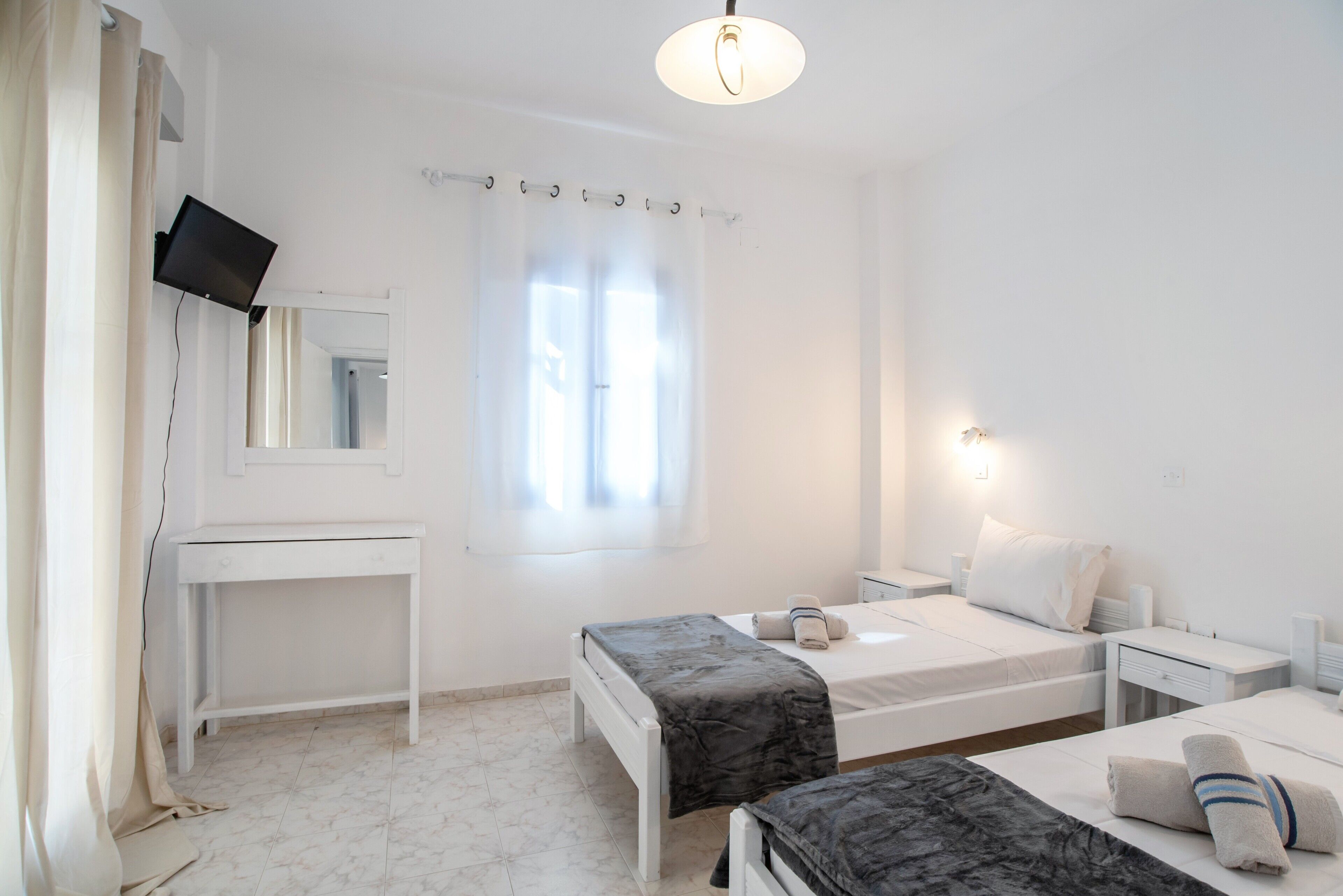 A hotel room with a bed, bedside tables, a desk, a mirror, and a window with curtains.