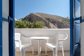 Un balcon ouvert avec des chaises et une table en plastique blanc, donnant sur une colline rocheuse.