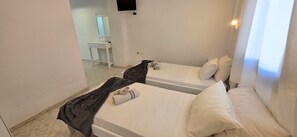 A hotel room with two single beds, a desk, a mirror, and a TV. - Economy Double Room 3 with Balcony and Air Conditioning (Perissa)