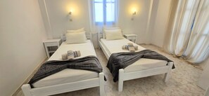 A hotel room with two single beds, white bedding, a dark throw blanket on one bed, and a small bedside table with a lamp. - Economy Double Room 3 with Balcony and Air Conditioning (Perissa)