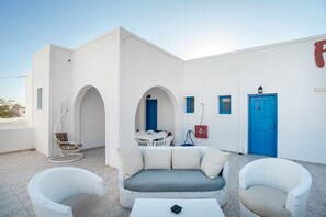 Un edificio blanco con una puerta azul, un sofá blanco y dos sillones de mimbre blanco.