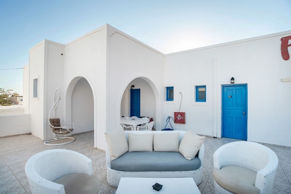 A white building with a blue door, a white sofa, and two white wicker chairs.
