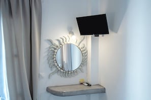 A bathroom with a vanity, a round mirror with a decorative frame, a mounted television, and a light fixture.