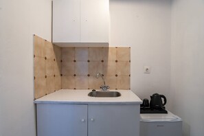 A small kitchenette with a sink, cabinets, and a kettle.
