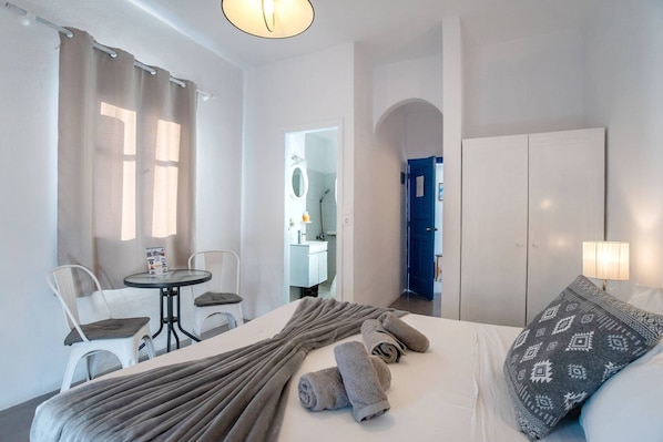 A hotel room with a bed, a table with chairs, a bathroom visible through an archway, and a wardrobe.
