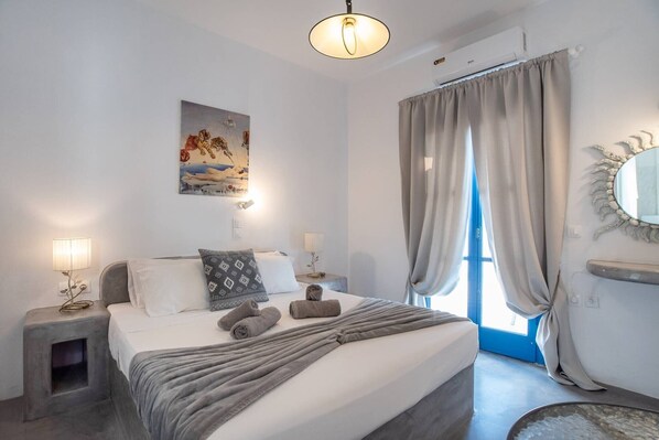 A bedroom with a bed, bedside lamps, a painting, and a window with curtains.
