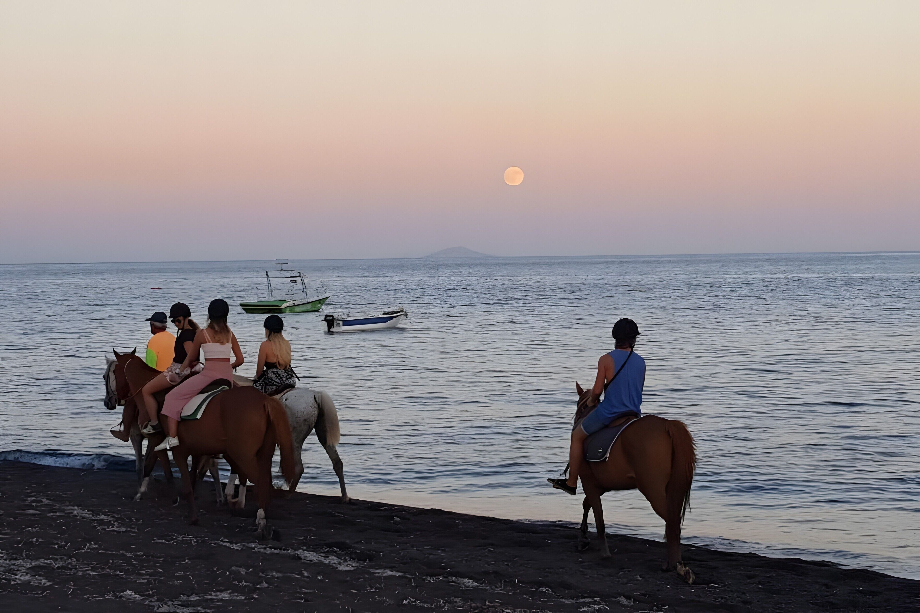 Une scène de plage avec des personnes à cheval et un bateau sur l’eau.