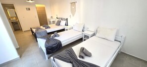 A hotel room with two beds, a small table, a chair, a bedside table, a mirror, and a bathroom with a sink and towel rack.