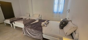 Une chambre dâhĂŽtel avec trois lits simples, une fenĂȘtre avec des rideaux et une porte.