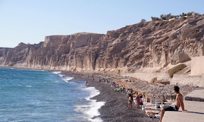 Ein Strand mit einer felsigen Klippe, Menschen liegen in der Sonne und Sonnenschirme sind aufgestellt.