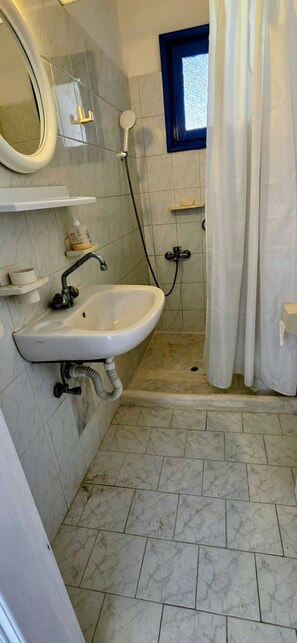 A bathroom with a sink, mirror, shower, and a window.
