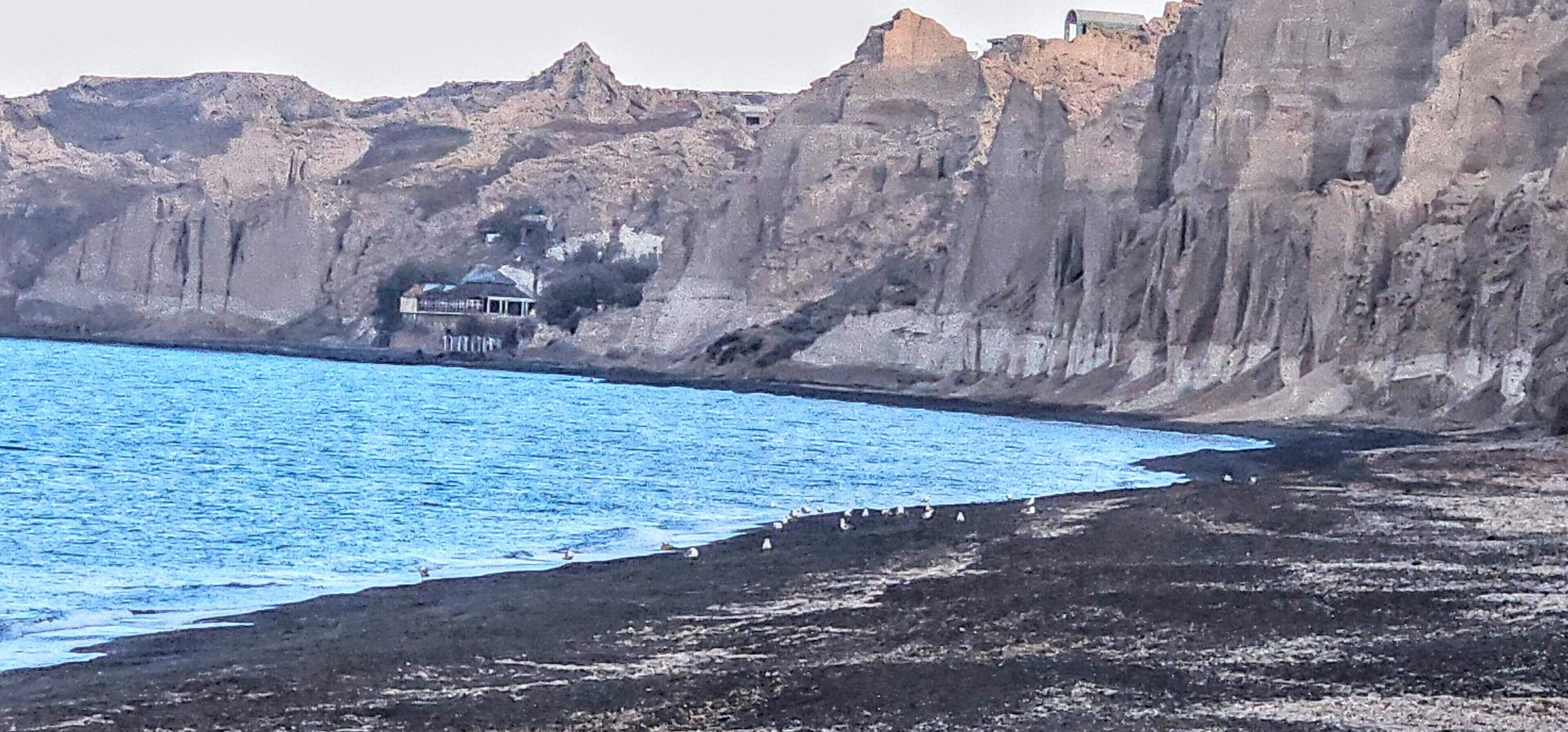 A coastal scene with a rocky cliff, a building with a white facade, and a beach.