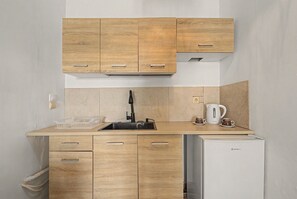 Une cuisine compacte avec des meubles en bois, un évier en acier inoxydable, une bouilloire et un réfrigérateur.