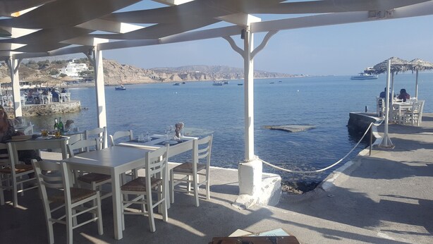 Ulkoterassi, jossa on pöytiä ja tuoleja, ja josta avautuu näkymä vesistöön. Kauempana näkyy myös veneitä.