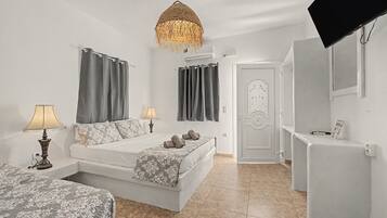 A bedroom with a bed, two bedside tables with lamps, a hanging light fixture, a door with a decorative handle, and a flat-screen TV mounted on the wall.
