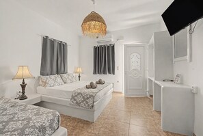 Une chambre à coucher comprenant un lit, deux tables de chevet avec des lampes, un luminaire suspendu, une porte dotée d’une poignée décorative et un téléviseur à écran plat fixé au mur.