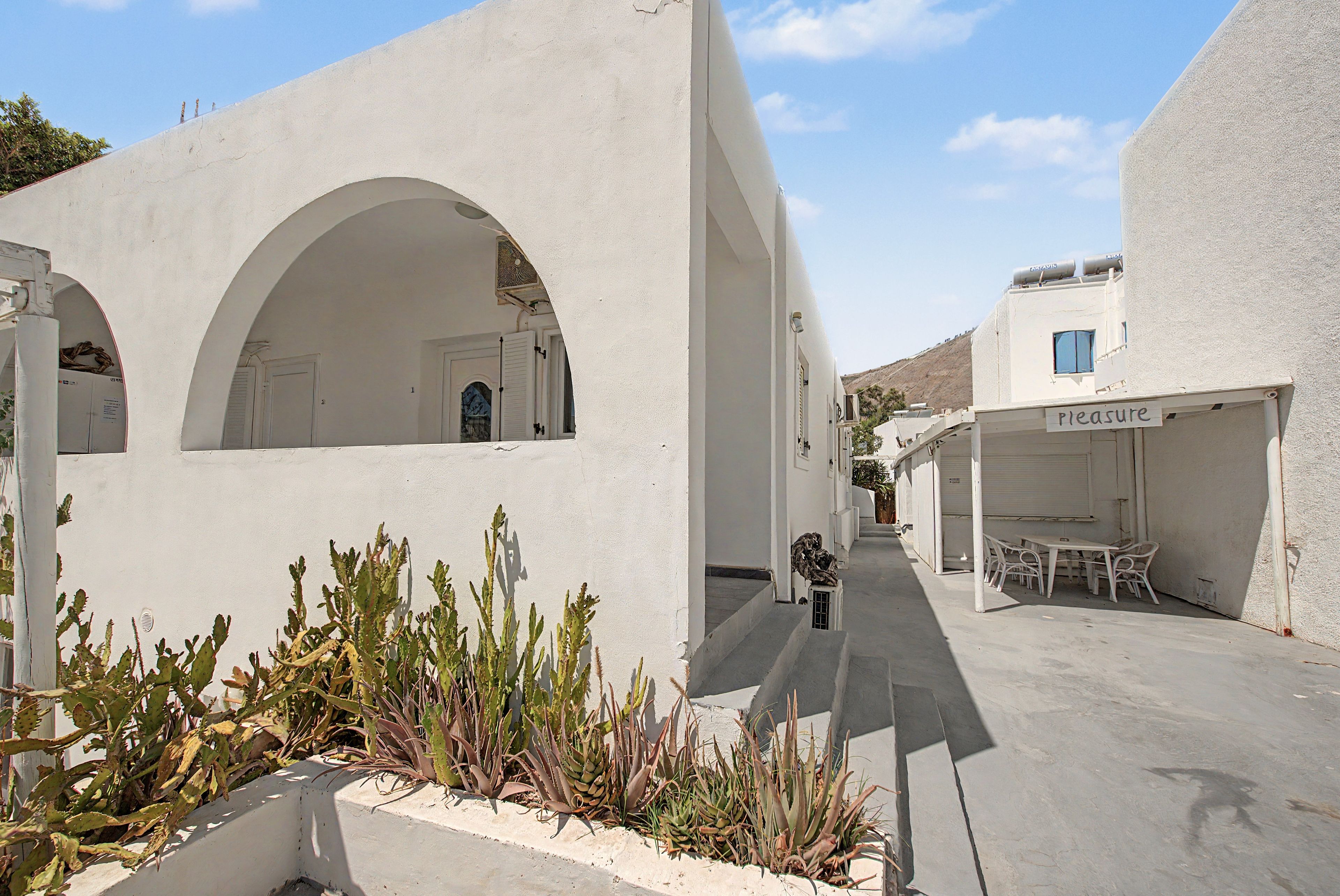 A narrow street with white buildings, arched doorways, and outdoor seating.