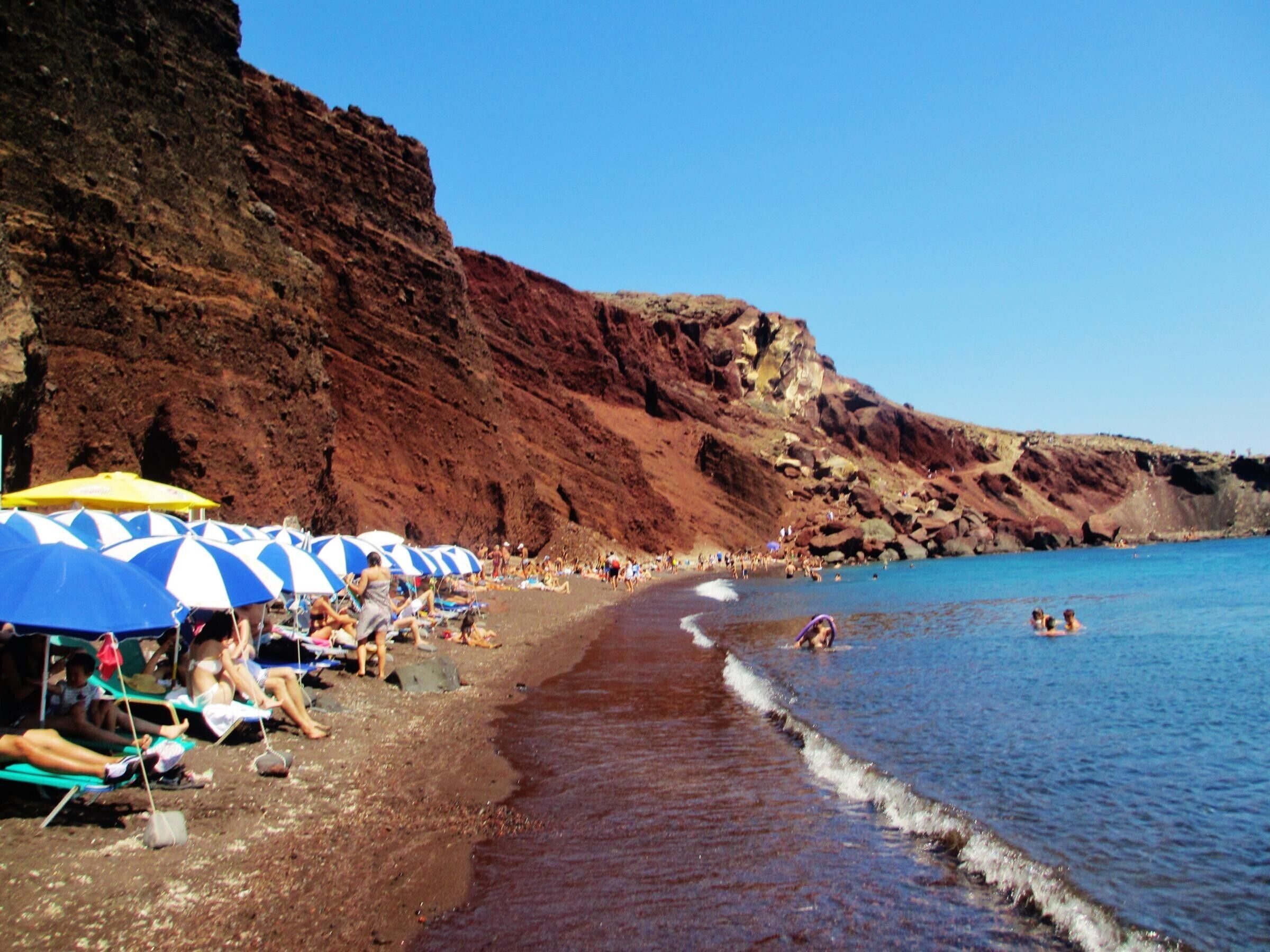 Une plage où des gens se prélassent au soleil, avec des parasols et une falaise rocheuse.