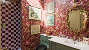 Une salle de bain avec un papier peint à motifs floraux, un carrelage à carreaux, un lavabo et des toilettes.