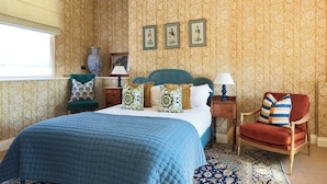 Une chambre à coucher avec un grand lit, une chaise, une table de chevet, une lampe et un vase.