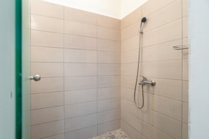 A small, tiled shower room with a handheld showerhead and a wall-mounted faucet.