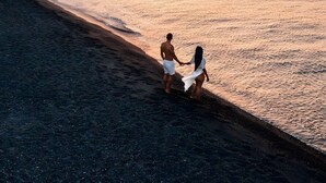 A beach scene with a couple holding hands, a sunset, and boats in the distance.