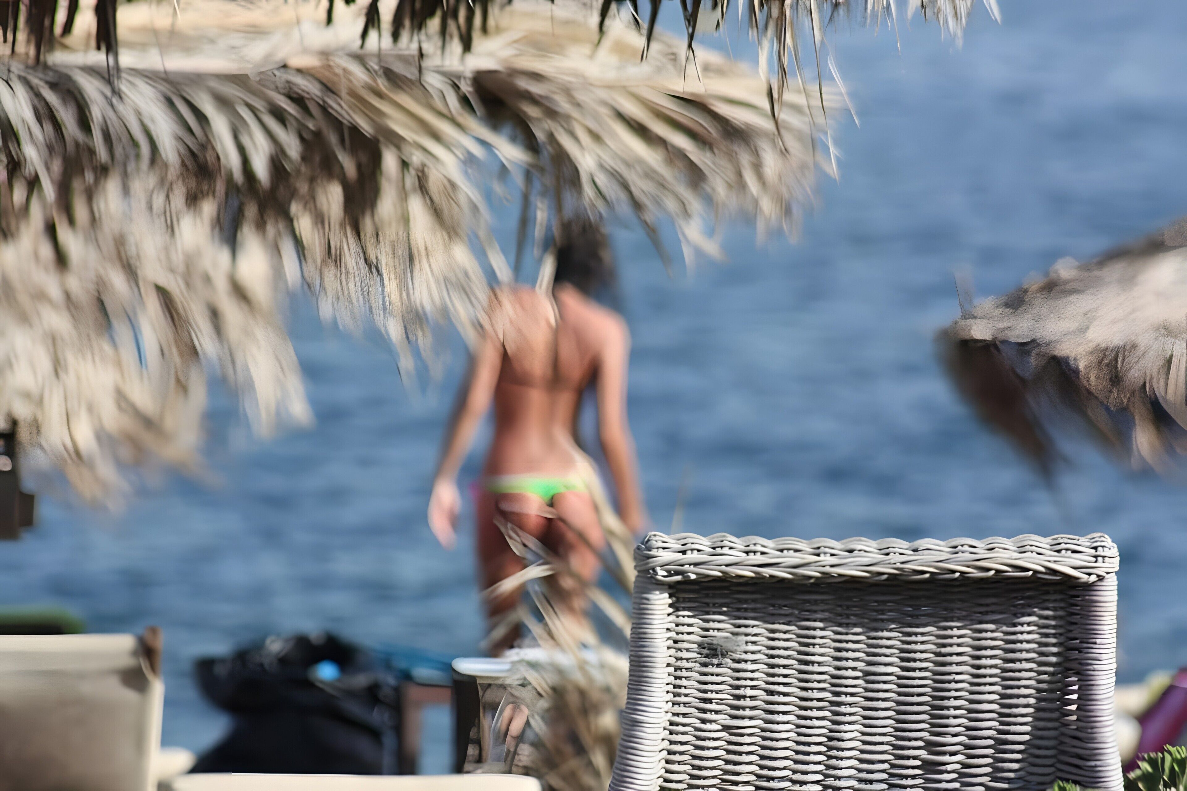 A beach scene with a wicker chair and a person in the background.