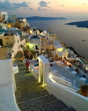 A coastal village with white buildings, a person on a balcony, and a view of the sea. - Two-Bedroom Apartment with Mountain View, Wi-Fi & Air Conditioning (Perissa)