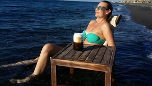 A person relaxing on a beach chair by the water with a drink on a small table. - Two-Bedroom Apartment with Mountain View, Wi-Fi & Air Conditioning (Perissa)