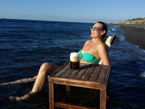 A person relaxing on a beach chair by the water with a drink on a small table. - Two-Bedroom Apartment with Mountain View, Wi-Fi & Air Conditioning (Perissa)