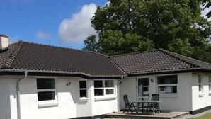 A single-story building with a tiled roof, a gravel driveway, and a small patio with outdoor seating. - 5 Star Holiday Home in Frederikshavn (Frederikshavn)