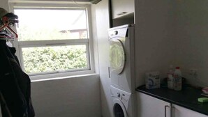 A laundry room with a washing machine, a dryer, a window, and a sink with cleaning supplies. - 5 Star Holiday Home in Frederikshavn (Frederikshavn)