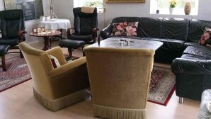 A living room with a black leather sofa, two armchairs, a coffee table, and a painting of a landscape. - 5 Star Holiday Home in Frederikshavn (Frederikshavn)