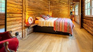 A log cabin bedroom with a bed, a red chair, and a wooden floor. - Spacious Wooden Chalet With Covered Terrace (Baarle-Nassau)