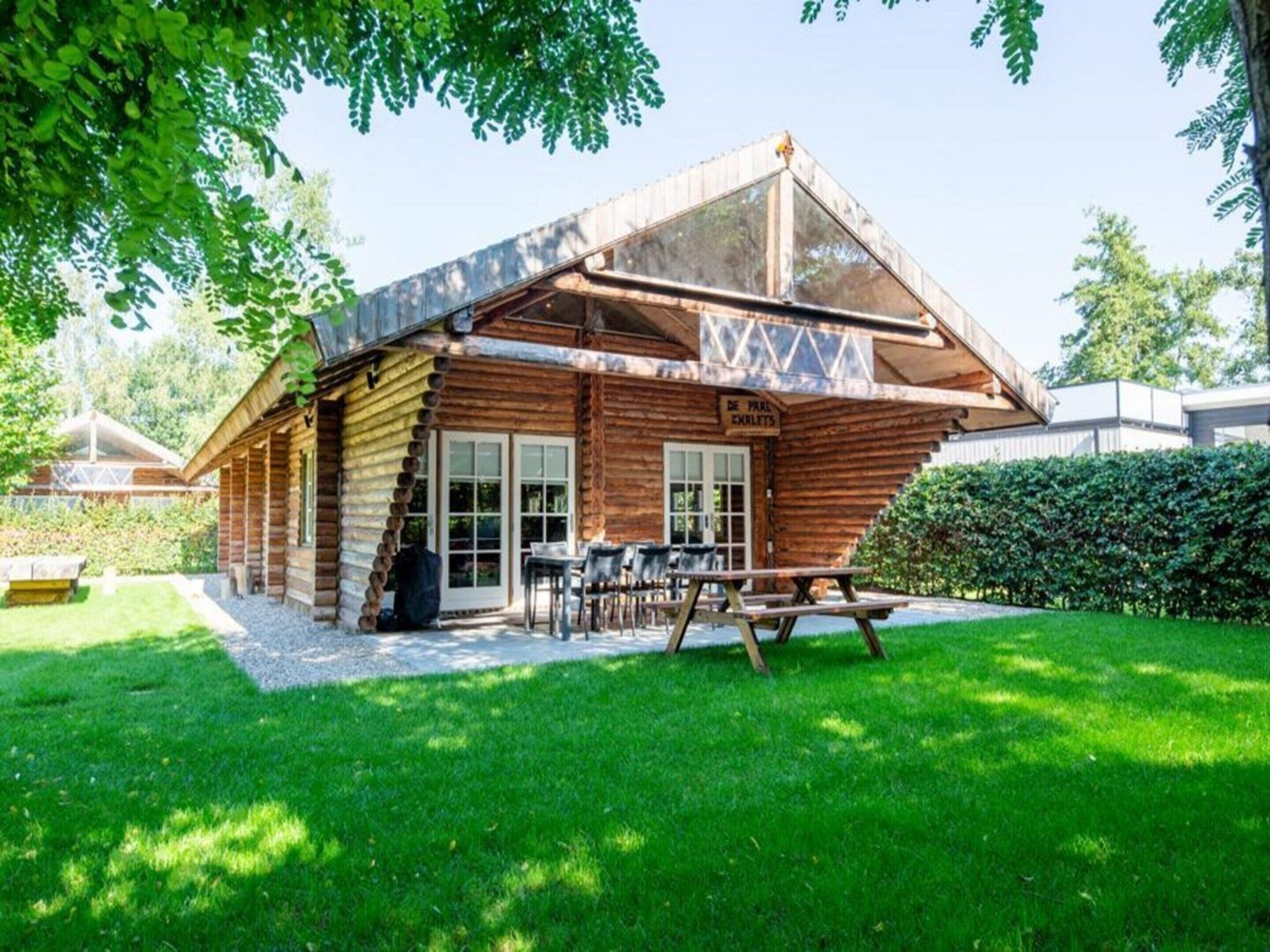 A log cabin with a glass extension, outdoor seating, and a sign reading "DE FRUIT EMKLETS".