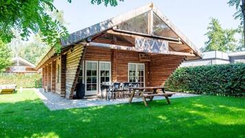 A log cabin with a glass extension, outdoor seating, and a sign reading "DE FRUIT EMKLETS".