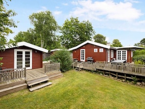 A wooden cabin with a deck, a barbecue area, and a covered outdoor seating area.