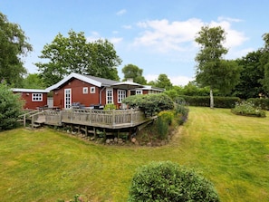 A red wooden house with a deck, a barbecue area, and a well-maintained lawn.