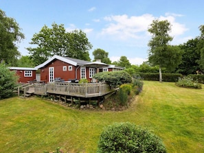 A red wooden house with a deck, a barbecue, and a grassy yard.