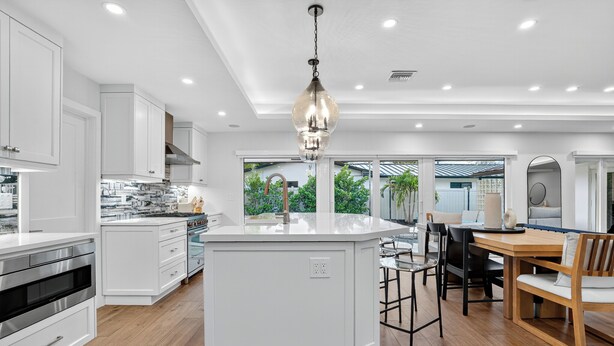 A modern kitchen with white cabinetry, a central island, and a dining area with a wooden table and chairs.
