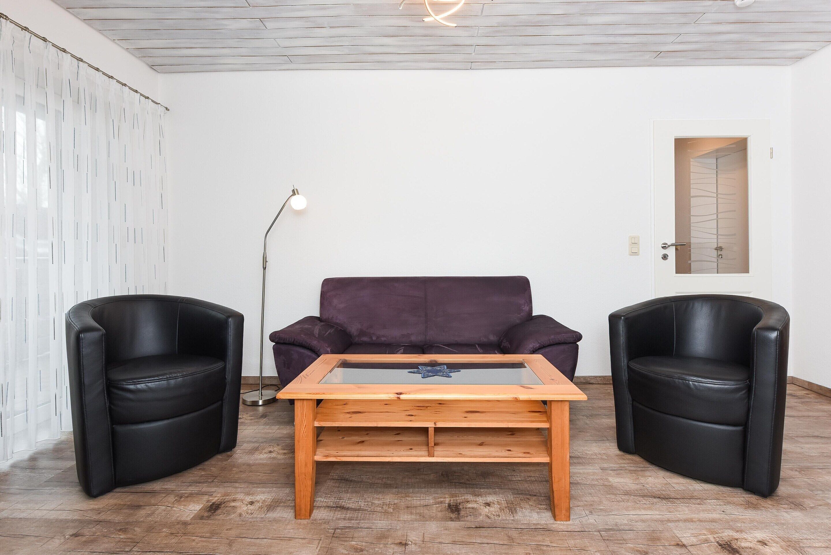 A room with a wooden coffee table, two black leather chairs, a purple sofa, and a floor lamp.