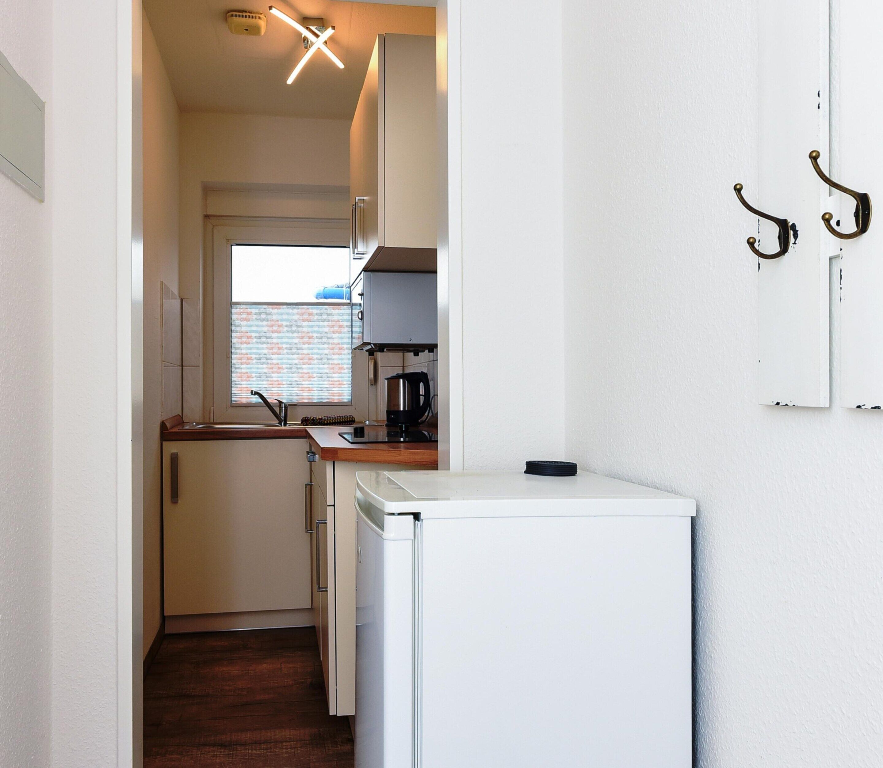 A compact kitchen with a refrigerator, a coffee maker, and a window with a view of a brick wall.