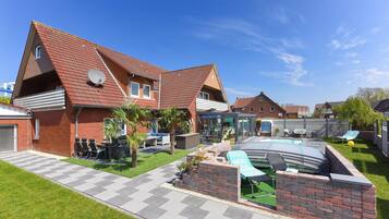A two-story house with a swimming pool, a patio with chairs, and a brick wall.