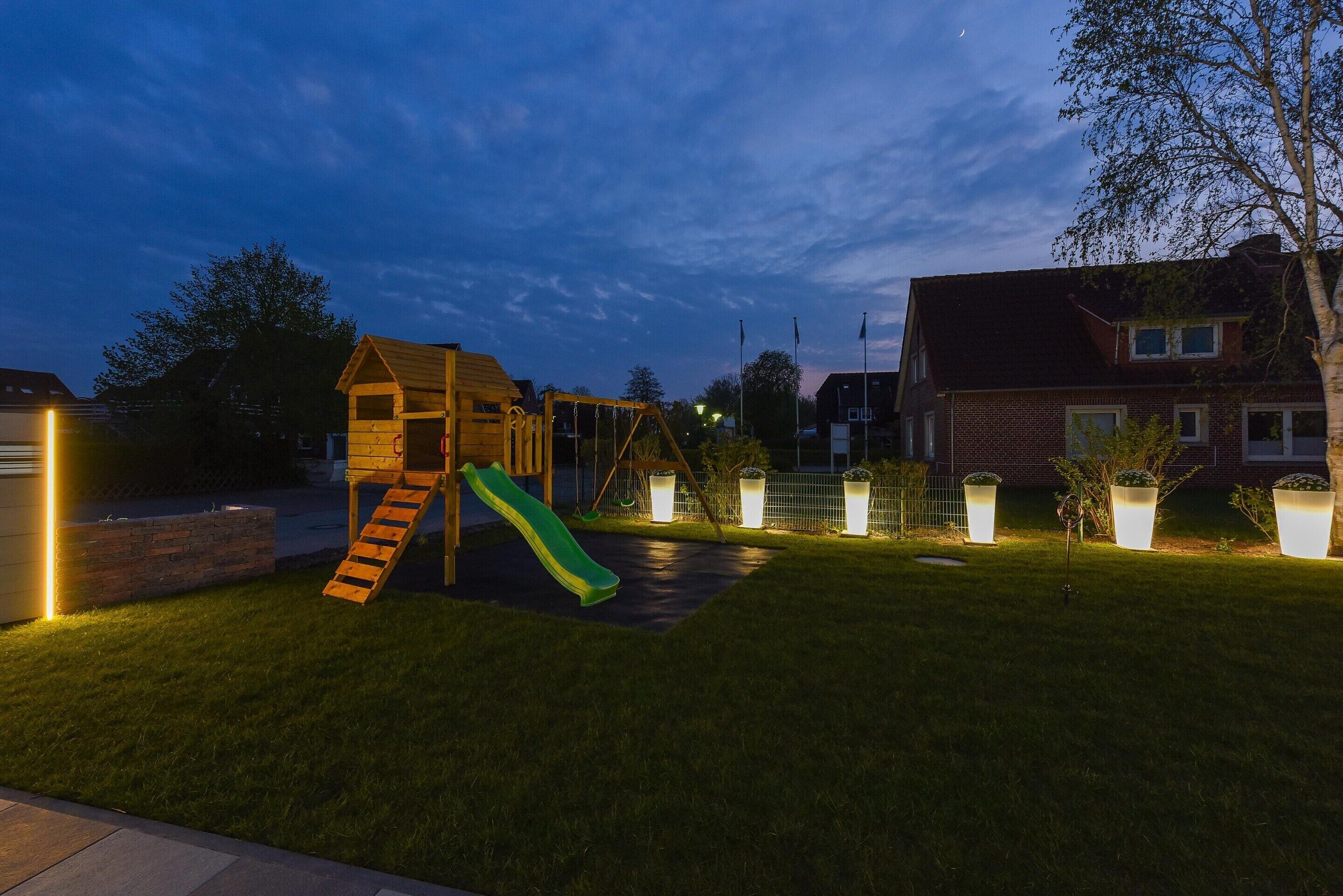 A backyard with a wooden playhouse and slide, surrounded by a well-maintained lawn and potted plants.