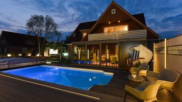 A modern house with a swimming pool, outdoor seating, and a well-lit patio area.