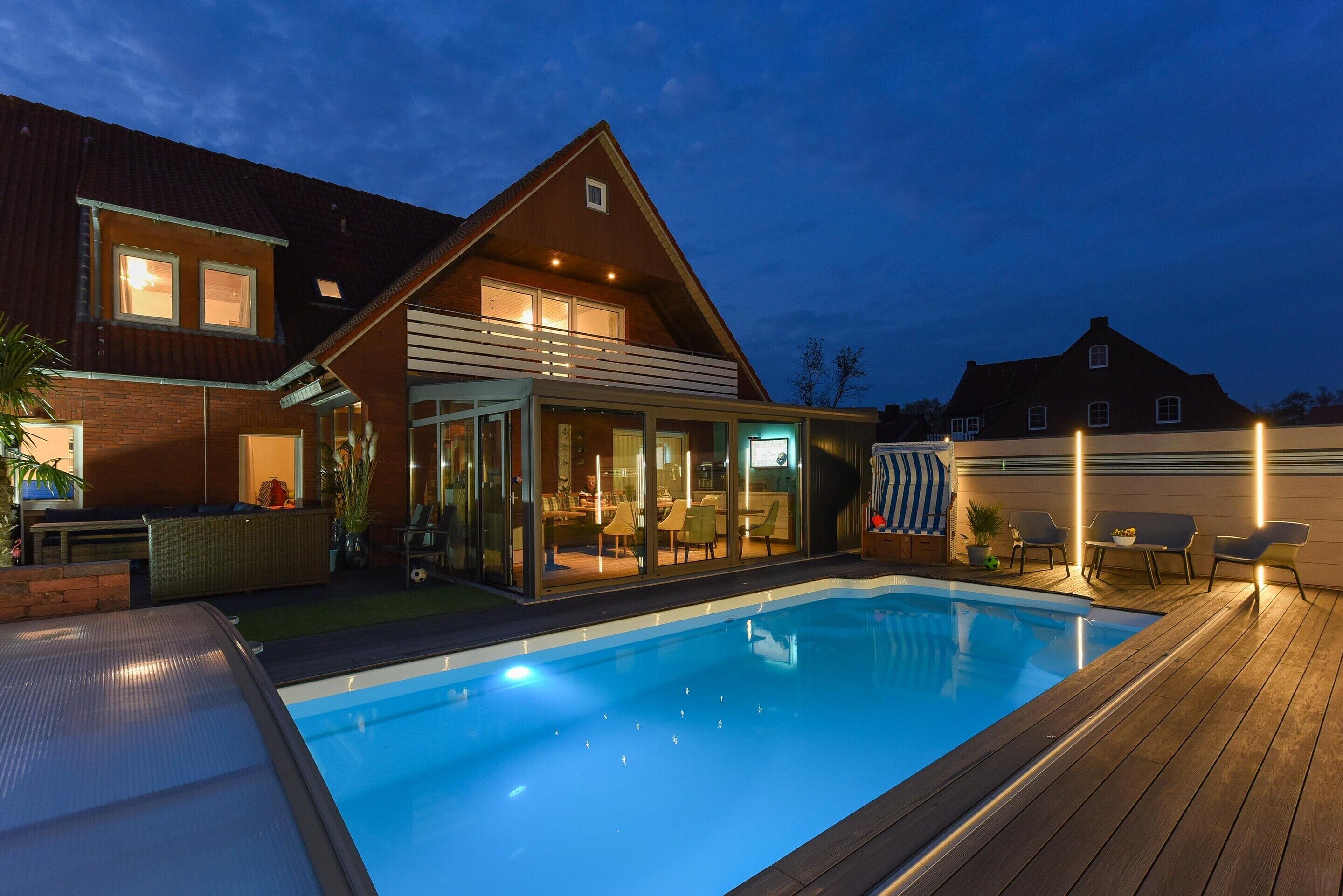 A modern house with a swimming pool, a covered patio, and a well-lit interior.