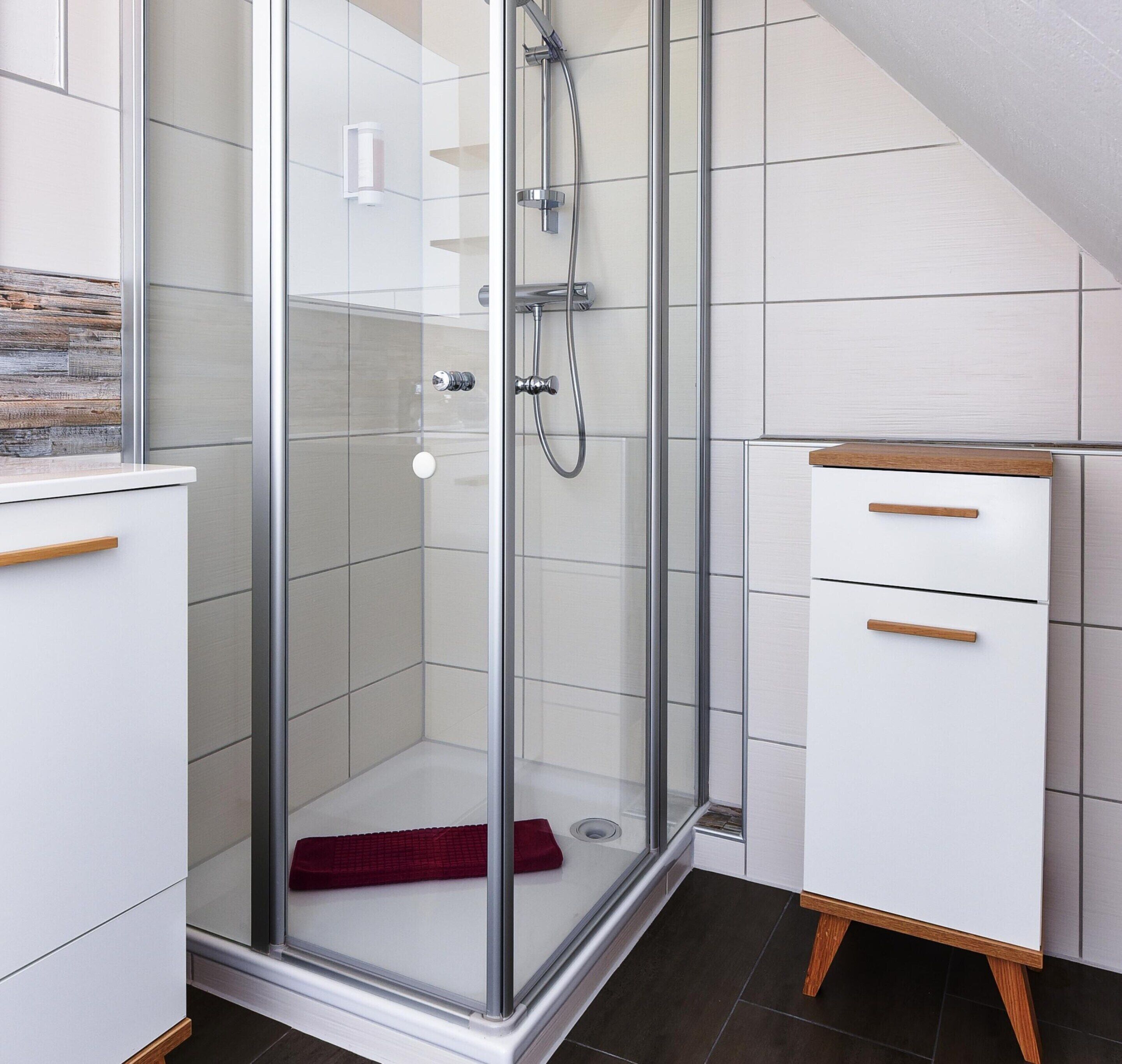 Een moderne badkamer met een glazen douchecabine, witte kastjes en een houten kast.