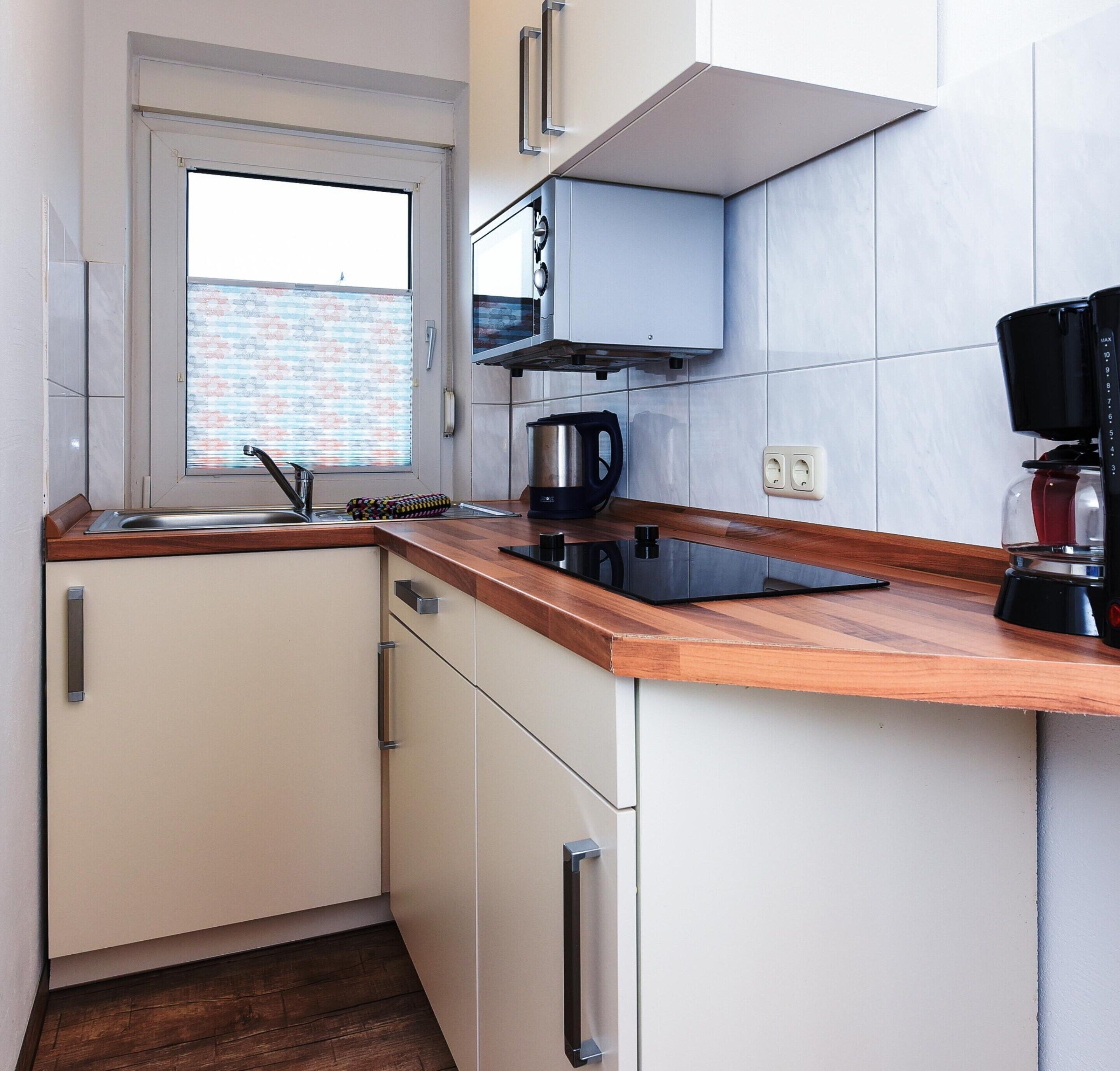 Une petite cuisine avec une fenêtre, une machine à café et une bouilloire posées sur le plan de travail.
