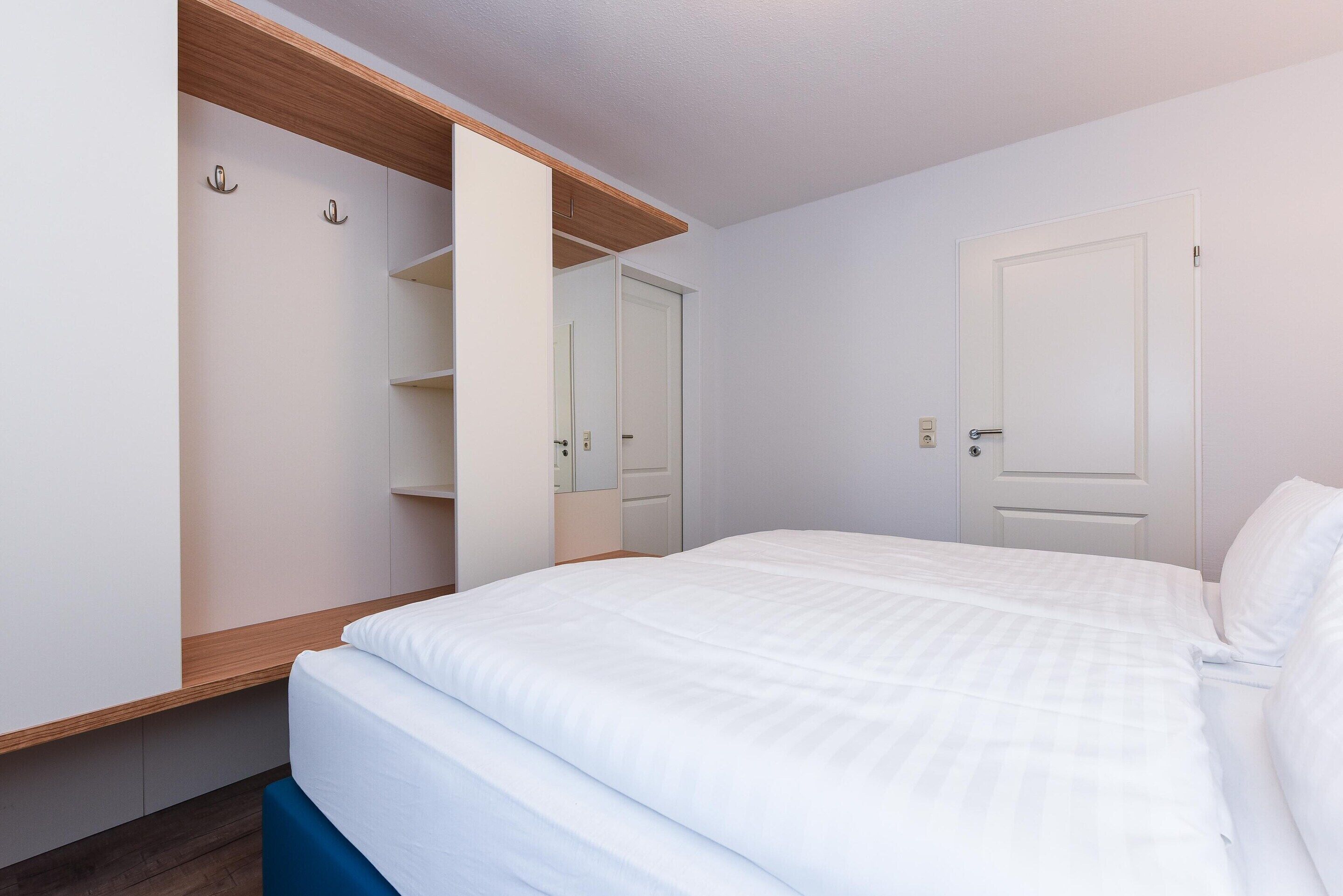 Un dormitorio con cama, armario abierto y una puerta a la derecha.