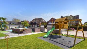 A residential area with a playground featuring a slide and swings, a brick patio, and a lawn.